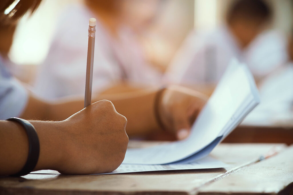 Closeup to hand of student holding pencil and taking exam in classroom with stress for education test.